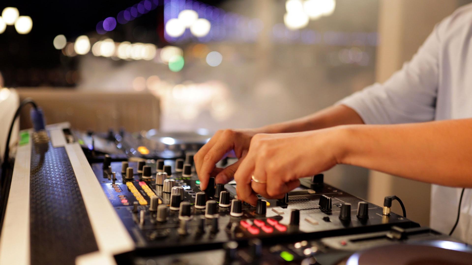 DJ Mixing Music on Professional DJ Mixer Under Glowing Lights at Nightclub – Close-Up of Hands Controlling Sound with Illuminated Equipment in a High-Energy Party Atmosphere